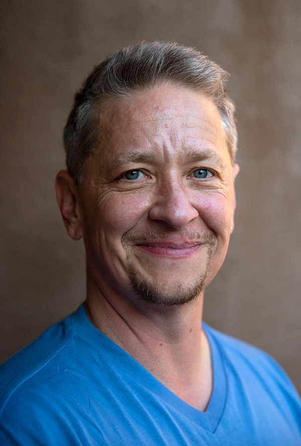 A white man with graying blonde hair and a short goatee wearing a blue shirt.